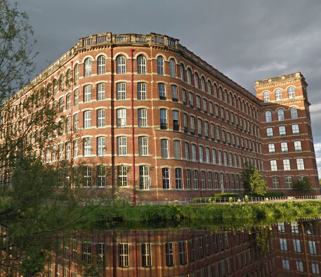 5-story red brick mill with white stone trim reflected in foreground pond