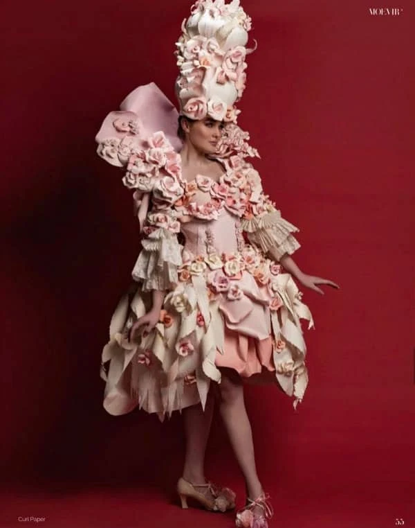 young female model, standing, dressed in elaborate dress and headpiece decorated with pink and cream paper flowers