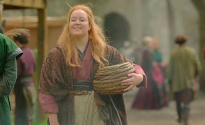 Una mujer vestida con ropas medievales lleva una cesta