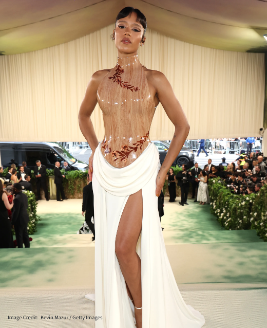 Photo of Taylor Russel at the 2024 Met Gala. She is wearing Loewe, a wooden-look bodice and cream flowy skirt with a thigh slit.