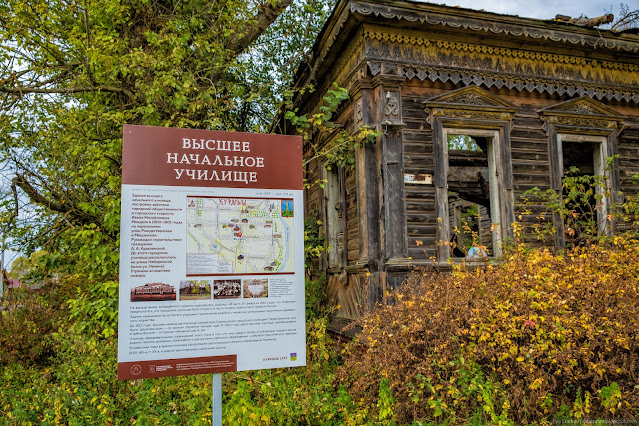 Информационный стенд на фоне руин деревянного здания