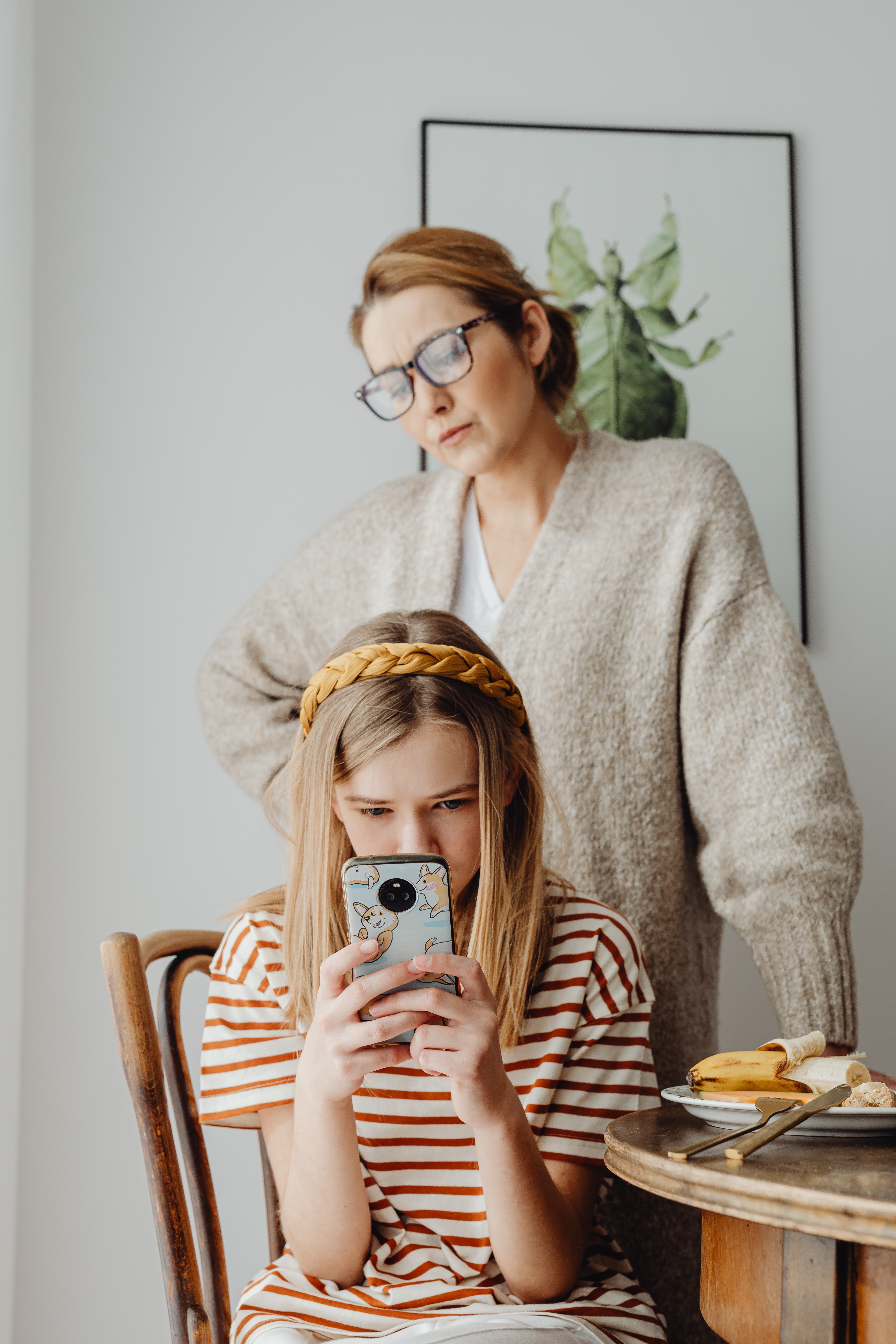 mom standing over daughter as daughter scrolls through phone