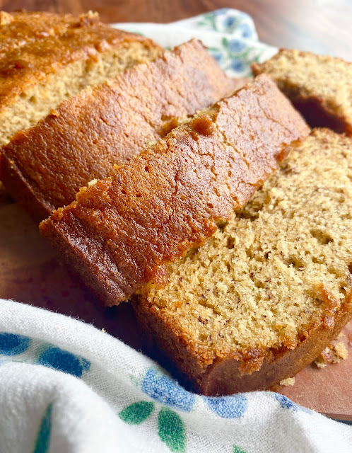 Close up of sliced Brown Butter Banana Bread on a wooden cutting board and tea towel.