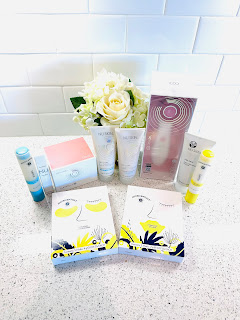 A collection of eight NU SKIN skincare products neatly arranged on a counter, accompanied by delicate white flowers, showcasing a blend of beauty and nature.