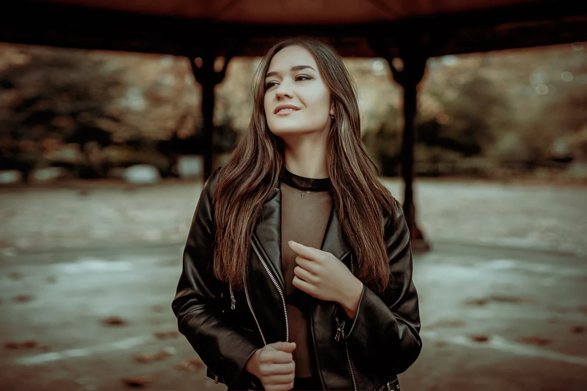 a beautiful, young woman with long brown hair is wearing a stylish leather jacket and poses for the camera