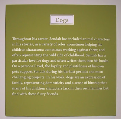 sign from museum that talks about sendak's love for dogs, text says, Throughout his career, Sendak has included animal characters in his stories, in a variety of roles:  sometimes helping his children characters; sometimes working against them; and often representing the wild side of childhood.  Sendak has a particular love for dogs and often writes them into his books. On a personal level, the loyalty and playfulness of his own pets support Sendak during his darkest periods and most challenging projects. In his work, dogs are an expression of family, representing domesticity and a sense of kinship that many of his children characters lack in their own families but find with these furry friends. 