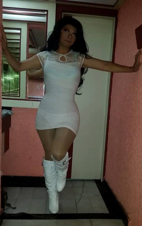 Sexy crossdresser wearing a tight white minidress with suntan pantyhose and white boots