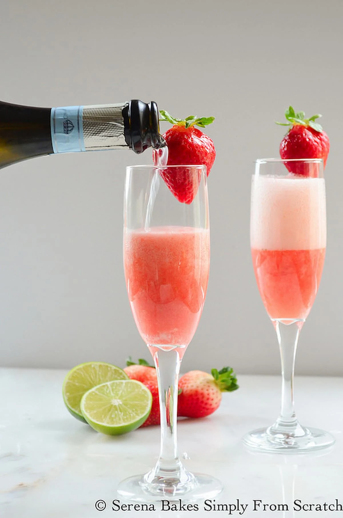 A Champagne Flute with pureed strawberries at the bottom being topped with champagne with a strawberry on the edge.