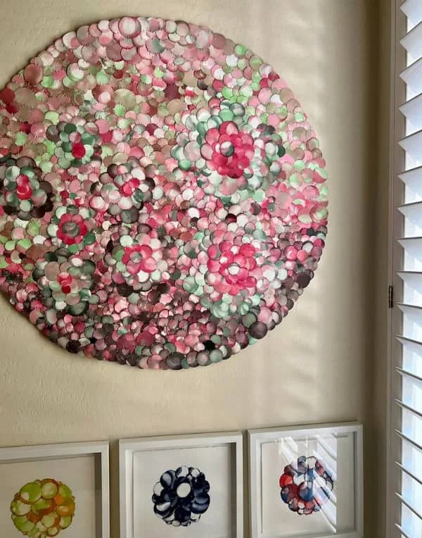 large-scale paper quilt composed of circles in shades of pink and green hanging on wall with smaller framed quilts on desk below