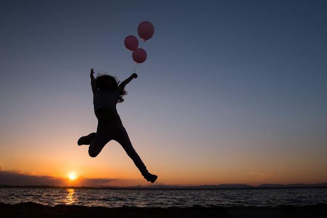 Niña en la orilla de la playa dando un salto con 3 globos atados de un hilo-