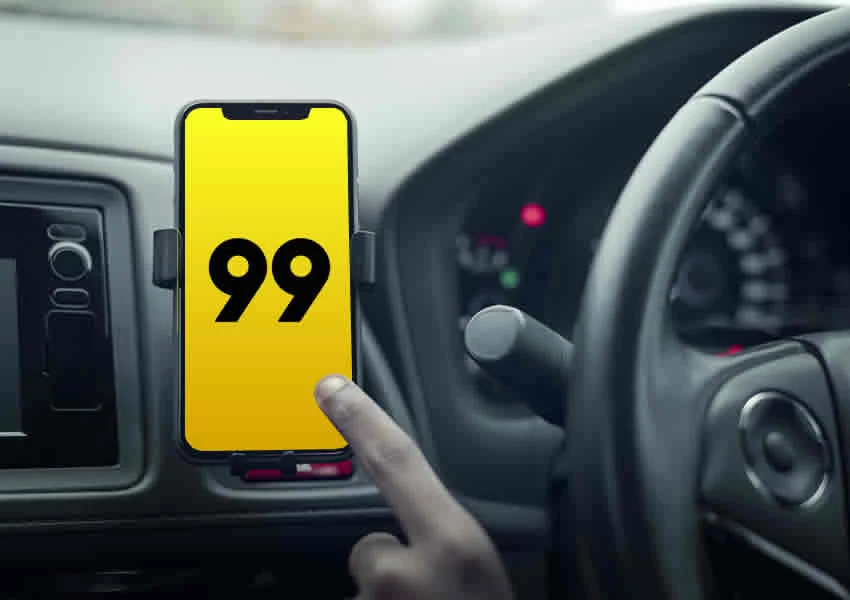 Imagem mostra uma mão clicando em um smartphone com o app da 99 aberto dentro de um carro.