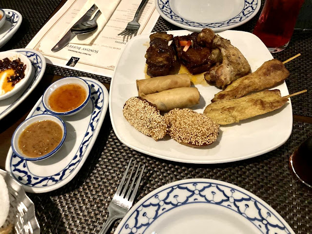 Plate of Thai starters including ribs, chicken satay, chicken wings, spring tolls and prawn toast, with two pots of sauce