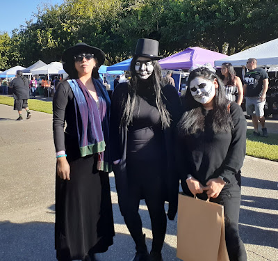A young woman dressed as a witch stands with two other women dressed as ghoulish characters.