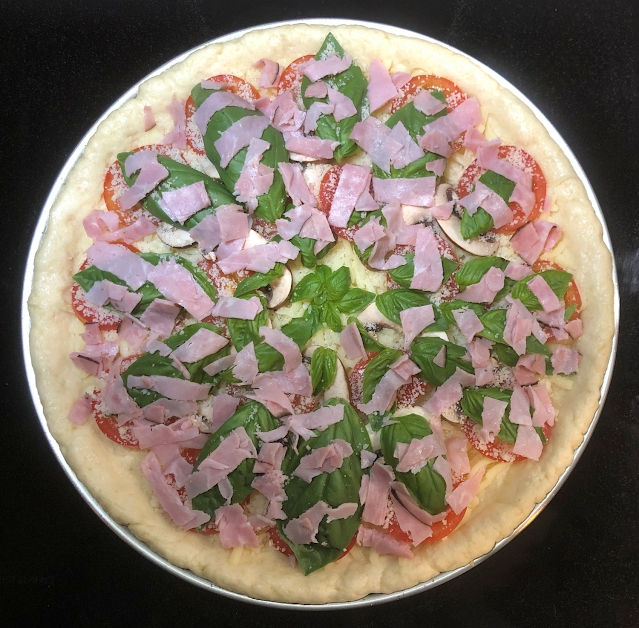 Keto pizza with mushrooms, tomatoes, ham and fresh basil before baking