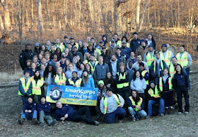 A group of AmeriCorps members stand together holding an AmeriCorps banner.