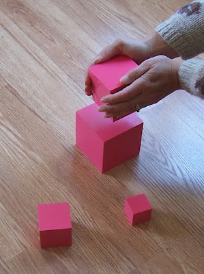 Lisa's hands holding and stacking a small pink cube on the Montessori Pink Tower
