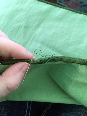 A close-up of a seam being whipstitched with kelly green thread. Both pieces are narrowly hemmed in deep apple green, with pale apple green lining.