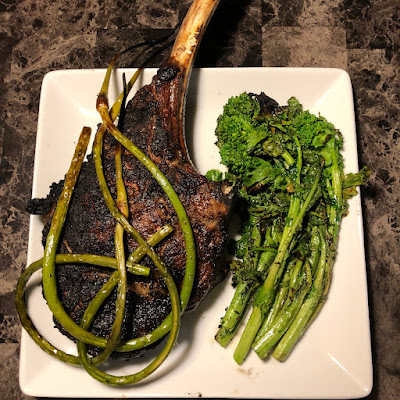 Prime tomahawk ribeye grilled Pittsburgh rare with grilled garlic scapes and broccoli rabe