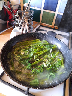 A frying pan full of asparagus with green leaves and shallow boiling water