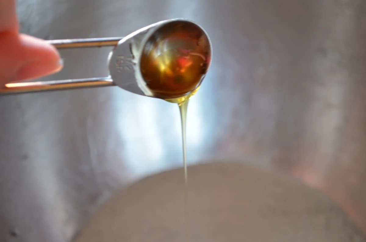 Honey drizzling off a measuring teaspoon into a bowl of water.