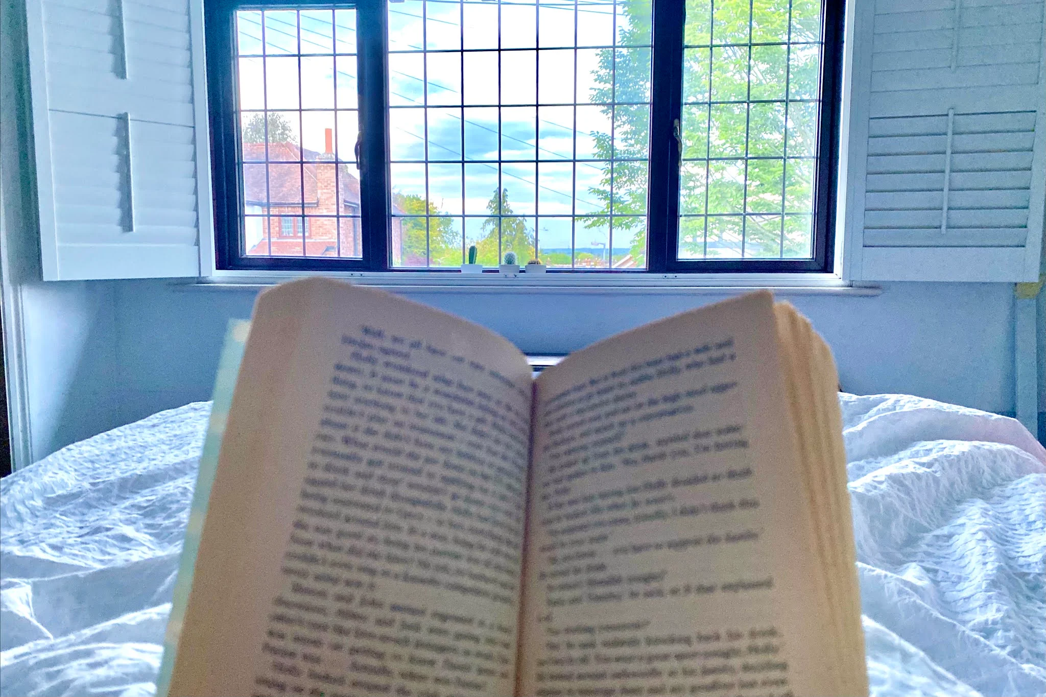 A view of a book being read in bed while looking out of the window one of the ways to recharge quickly as a parent.