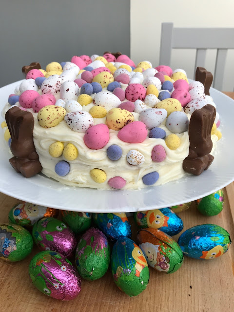 A cake covered in frosting, mini eggs and chocolate bunnies