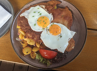 A large Schnitzel on top of roast potatoes, with two eggs on top