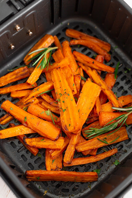 carrots in an air fryer basket garnished with rosemary.