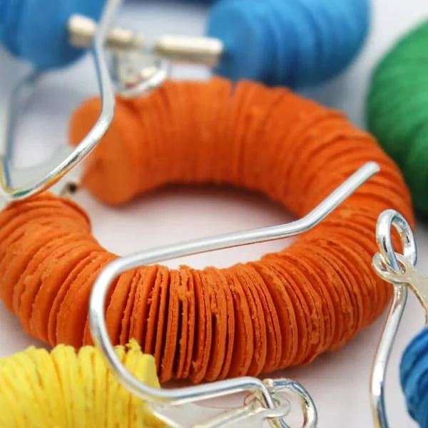 circular earring composed of orange paper discs with silver findings displayed with similar earrings in an array of colors.