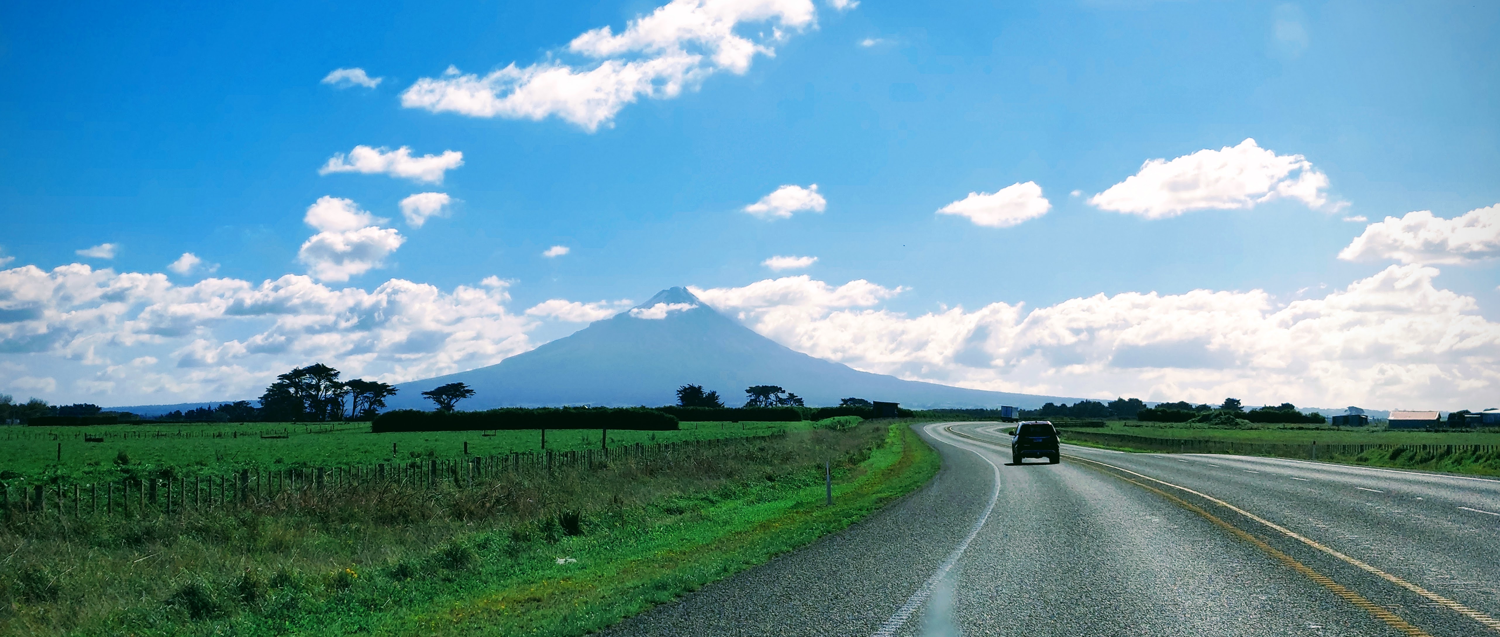 Driving the flat countryside of the Taranaki region with the slopes and peak of Mt Taranaki in the distance