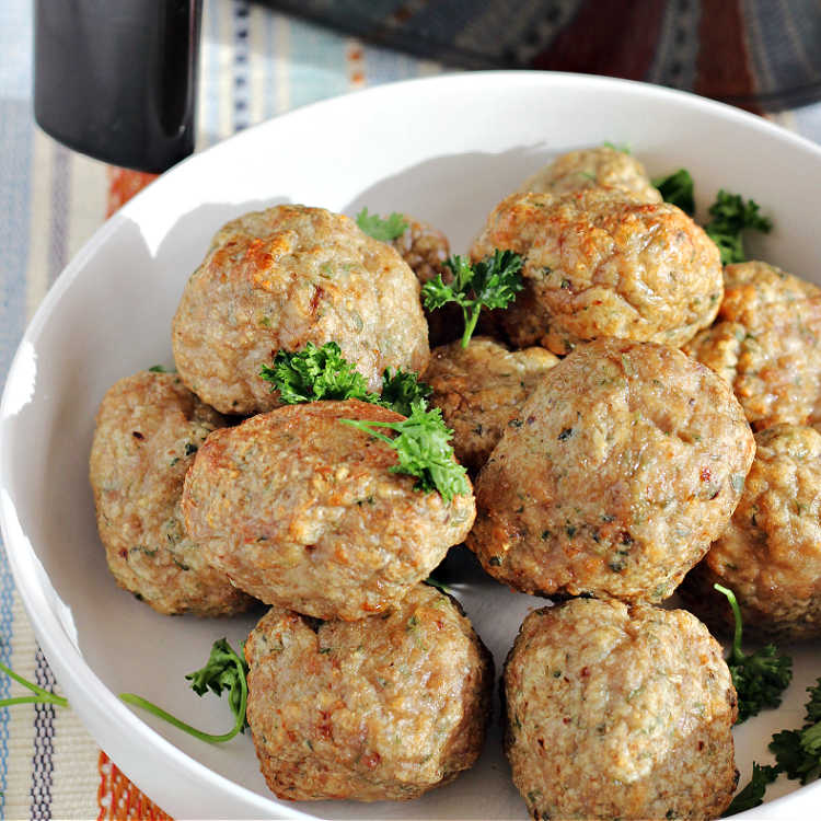 Bowl of air fryer turkey meatballs ready to eat sitting in front of an air fryer and garnished with fresh parsley