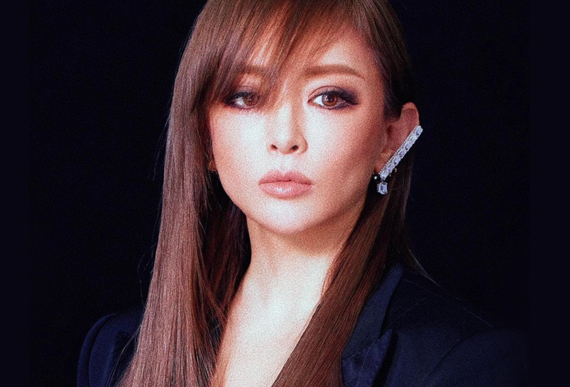 A grainy shot of Ayumi Hamasaki with long, straight, chestnut coloured hair. Wearing a black blazer and a silver bejewelled bar for an earring.