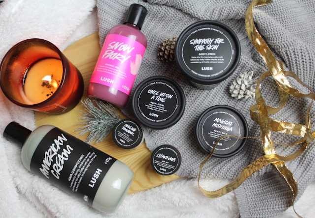 A pile of different LUSH products in a flatlay next to a candle