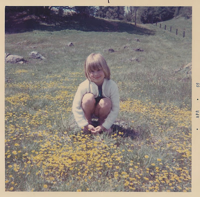 Photo of Lisa Nolan as a young child, wearing a white sweater and sitting in a field of daisies