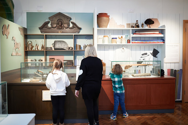 Two children and an adult looking at recreated displays of a Victorian ironmonger and a drapers. There are lots of original objects on display.