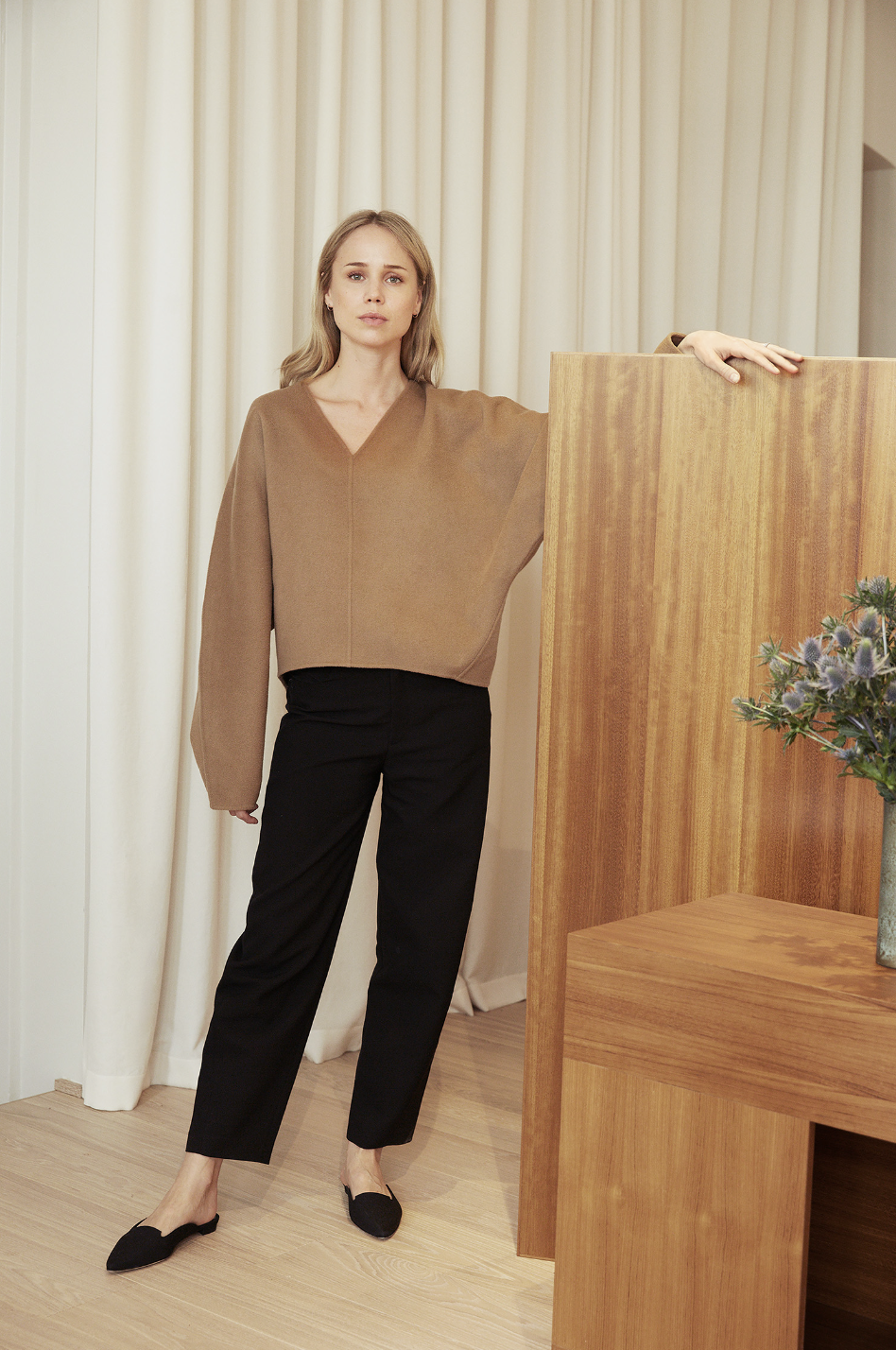 3-Piece Office Outfit for Spring — Elin Kling in a camel v-neck sweater, black pants, and black mule flats.