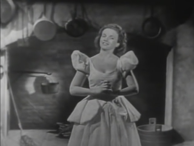 black & white screenshot of Ilene Woods in a white dress with puffy short sleeves and big skirt similar to Disney's Cinderella's, singing in front of a stage version of Cinderella's fireplace, from Perry Como Show in 1950