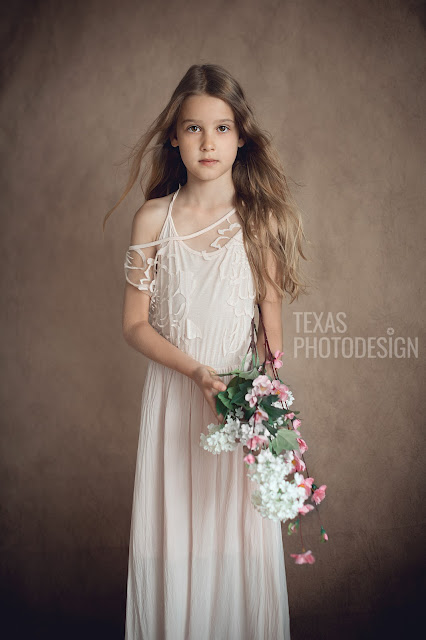 Sprookjesachtige foto van een meisje met golvende, lange haren en een dromerige jurk aan en ze houdt bloemen vast.
