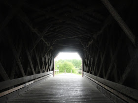 covered bridge, from dark interior, view of tree in sunlight at the end