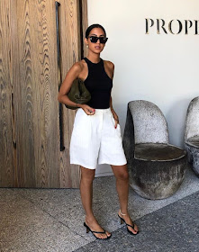 How to Wear White Shorts for Summer — Tania Sarin in black sunglasses, a racerback tank top or bodysuit, a pouch clutch, long white shorts, and heeled flip-flop sandals