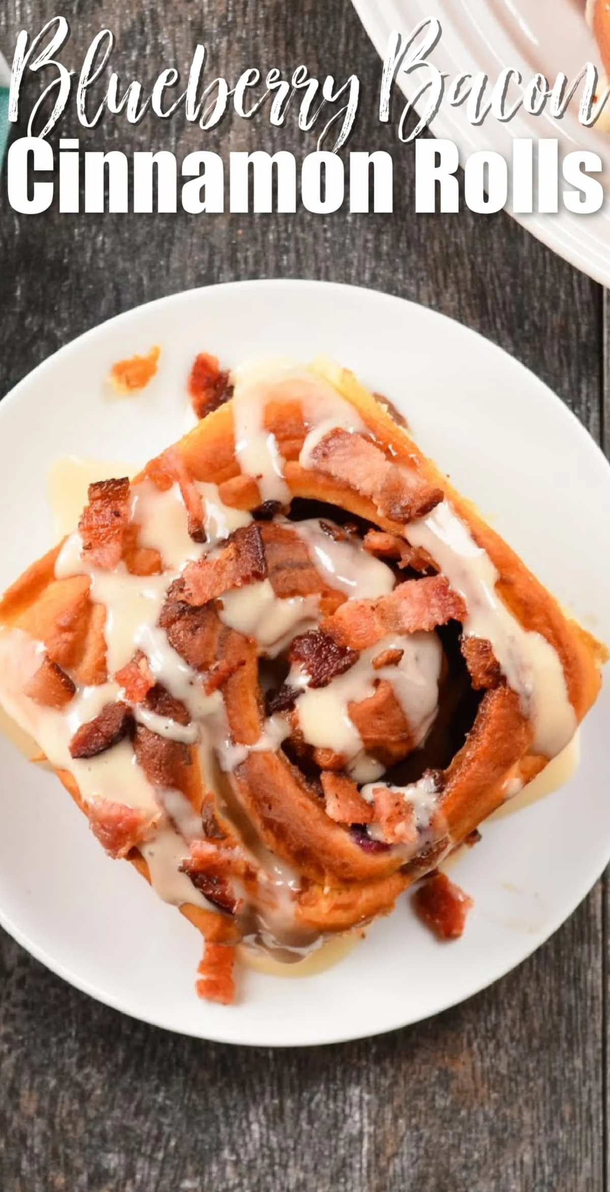 Blueberry Bacon Cinnamon Roll drizzled with Maple Cream Cheese Frosting on a white plate with white text at the top Blueberry Bacon Cinnamon Rolls.