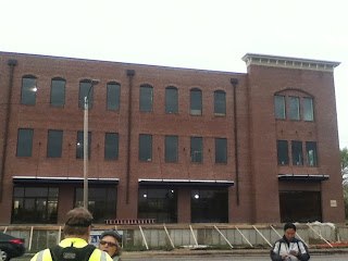 people in bike gear in front of three-story brick building under construction