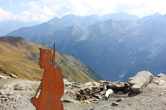 Nad przełęczą Stelvio, wokół szczytu zwanego Drei Sprachen Spitze lub Cima Garibaldi, znajdują się pozostałości okopów z I wojny światowej. Dziś towarzyszą im tablice informacyjne oraz metalowe figury żółnierzy. Brązowa, pordzewiała figura żółnierza z bagnetem na ramieniu - wycięta w metalowej, cienkiej blasze, stoi na kamiestym szczycie. W tle widoczne są wysokoalpejskiej szczyty grupy Ortles-Cevedale, powoli zakrywane nadciągającymi chmurami.