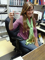 White woman with long blondish brown hair holds up cup in a "cheers" type gesture