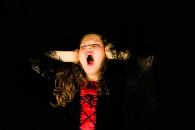 An image of a girl wearing a black and red dress  covering her ears with the hands and shouting with the black background- sad girl dp
