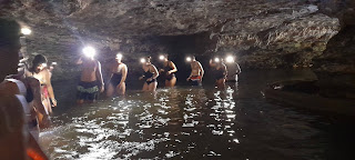 Turistas aventurándose en las Cavernas Jumandy, cruzando aguas y cascadas subterráneas con linternas y formando un camino en medio de la oscuridad para descubrir la maravilla subterránea.