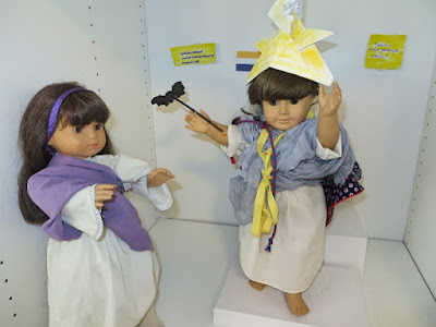 American Girl doll in white nightgown with light purple cloth robe over one shoulder, purple ribbon headband, silver paper sword in hands, American Girl doll representing Columbia (same as above)