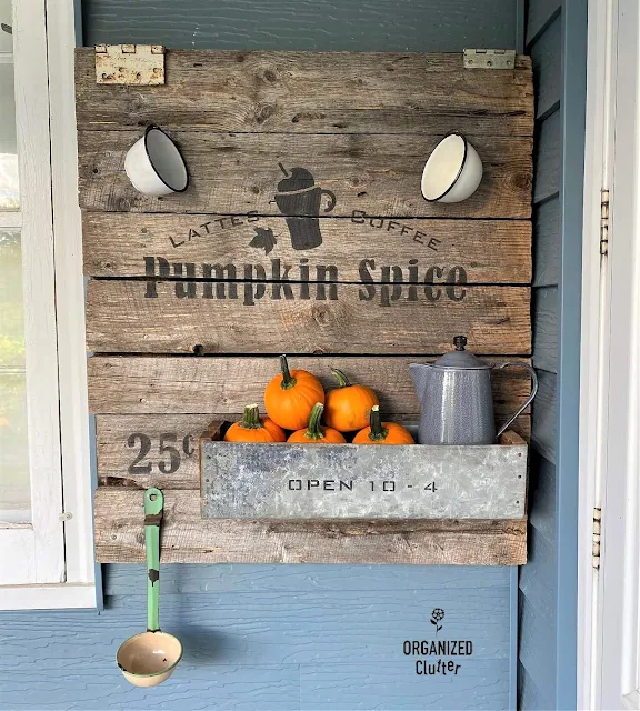 Photo of a barn door pumpkin spice latte sign with enamelware cups, galvanized drawer with pumpkins & a coffeepot, and a ladle/dipper.