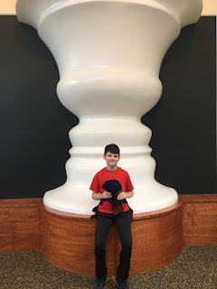 Boy sitting in front of a huge white vase, the negative space around which defining face profiles looking at eachother