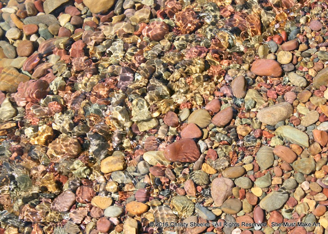 Colorful pebbles in the shallow water at the shore's edge.